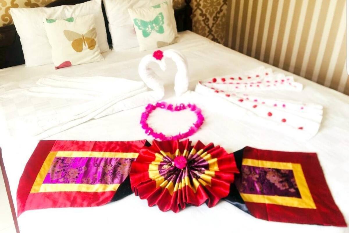 A neatly made bed with decorative pillows, a swan-shaped towel, a heart-shaped towel, and a colorful cloth.
