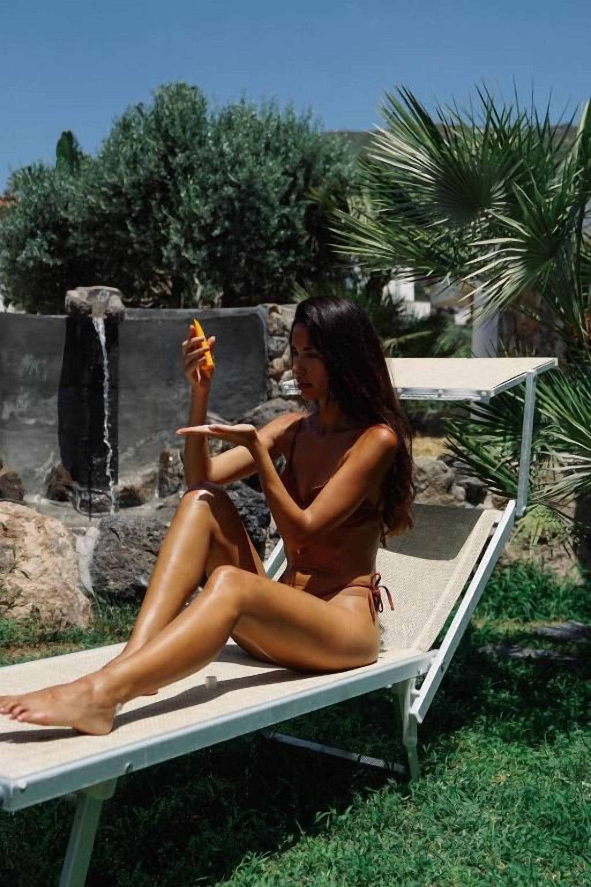 Una persona sentada en una silla de descanso al aire libre, con una piscina al fondo.