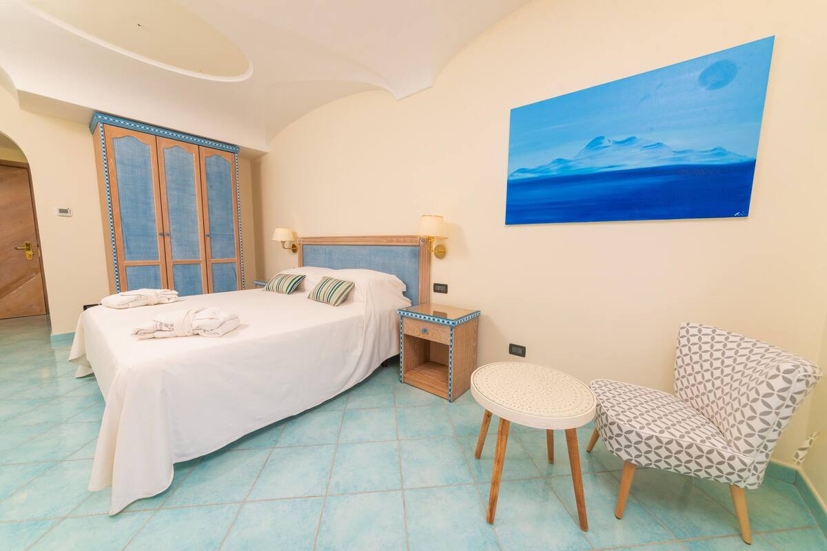 Un dormitorio con cama, mesita de noche, silla y un cuadro en la pared.