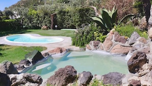 A landscaped garden with a swimming pool, rocks, and greenery.