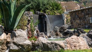 A rock garden with a water feature, including a waterfall and a pond, surrounded by large rocks and greenery.