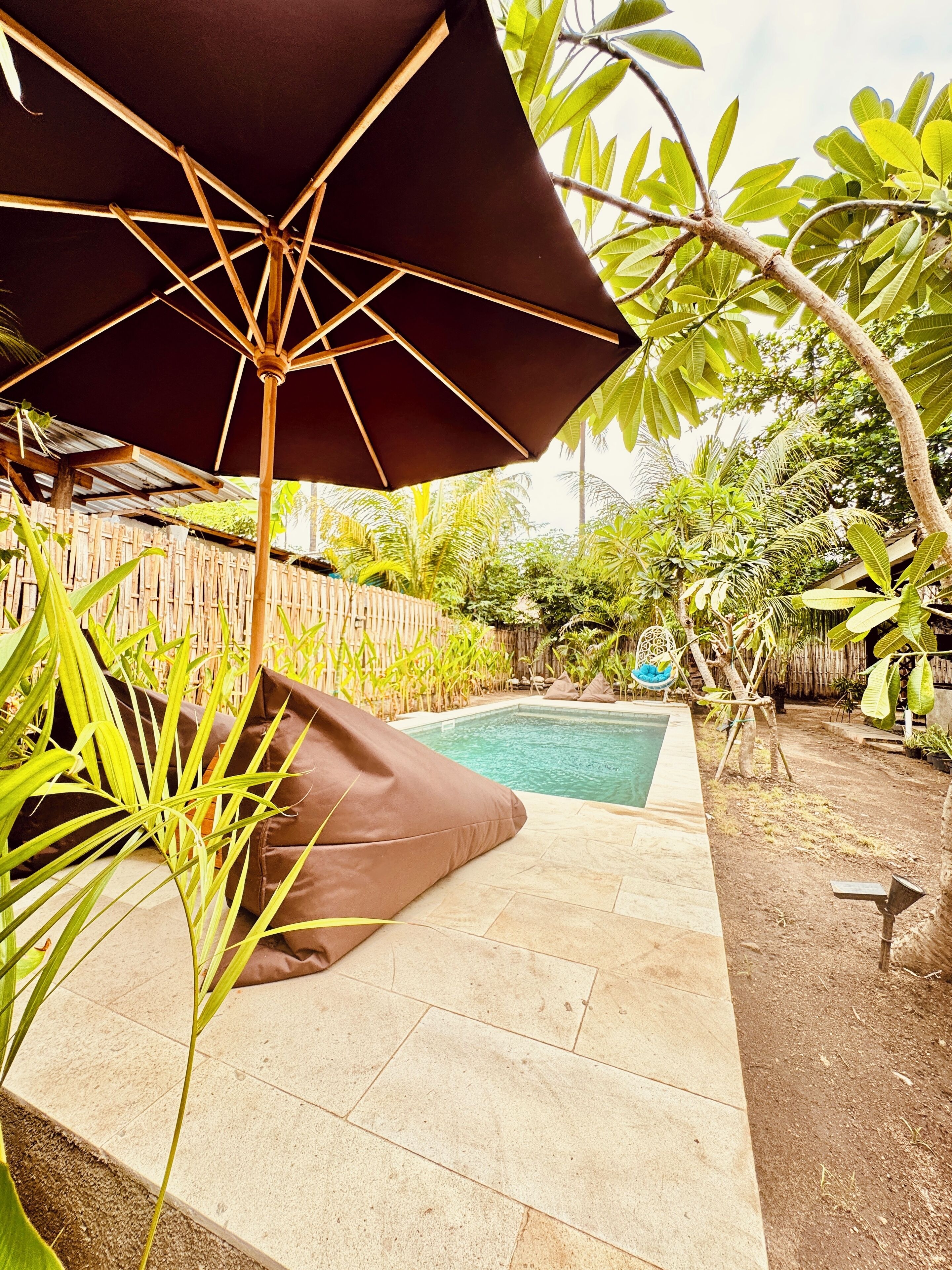 A poolside area with a wooden deck, a black umbrella, and a brown cushion.