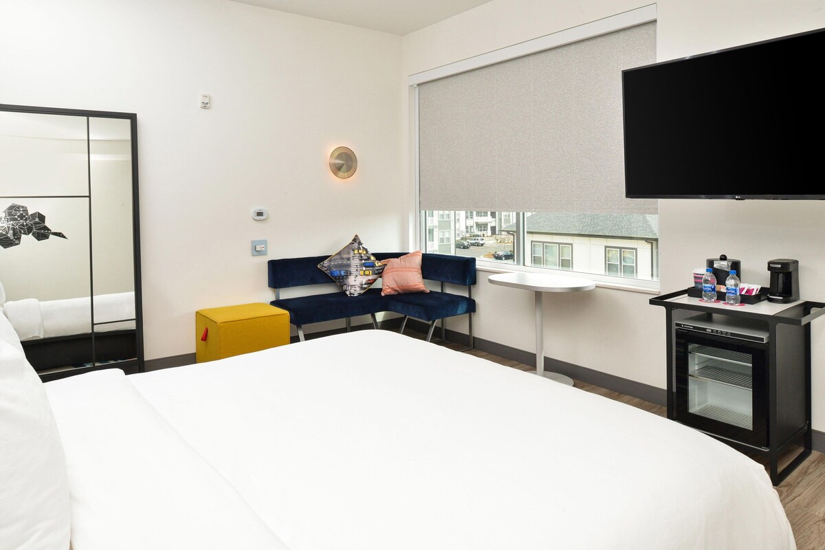 Una habitación de hotel con cama, sofá, una mesita, televisor y un minibar.