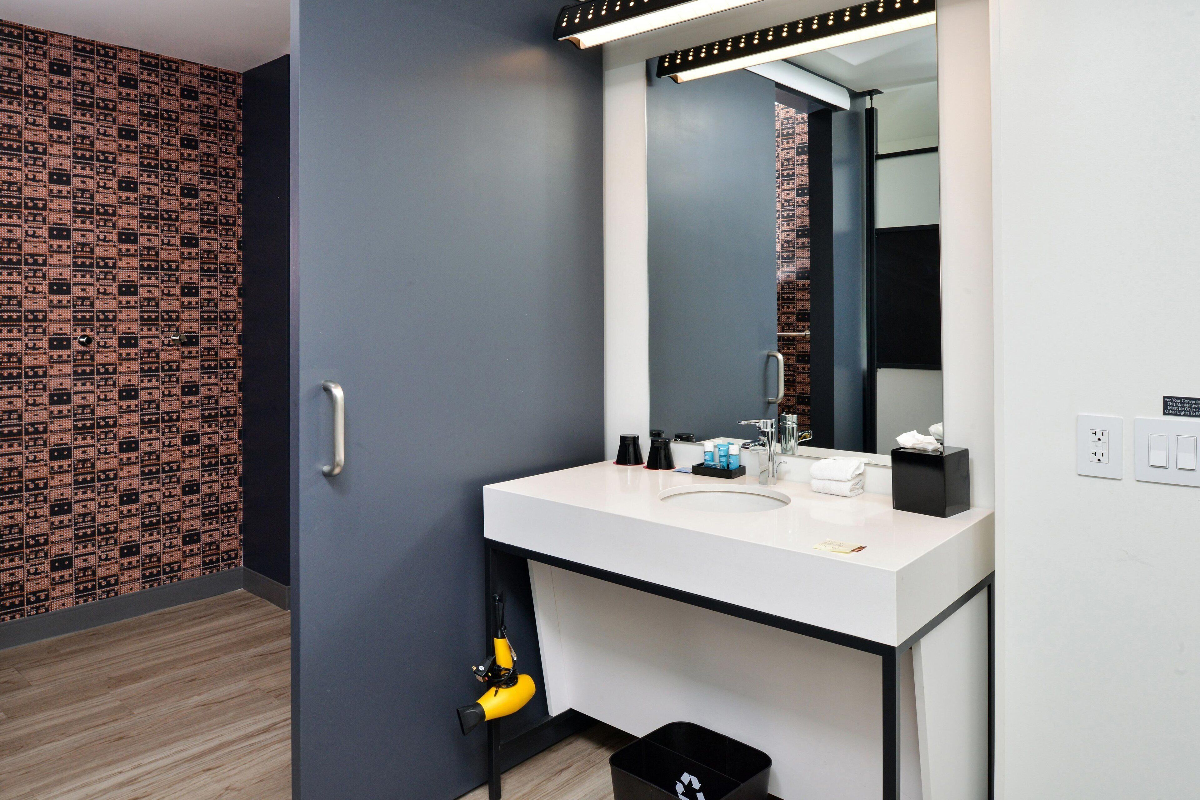 Une salle de bain moderne avec un lavabo blanc, un miroir et une poubelle noire.