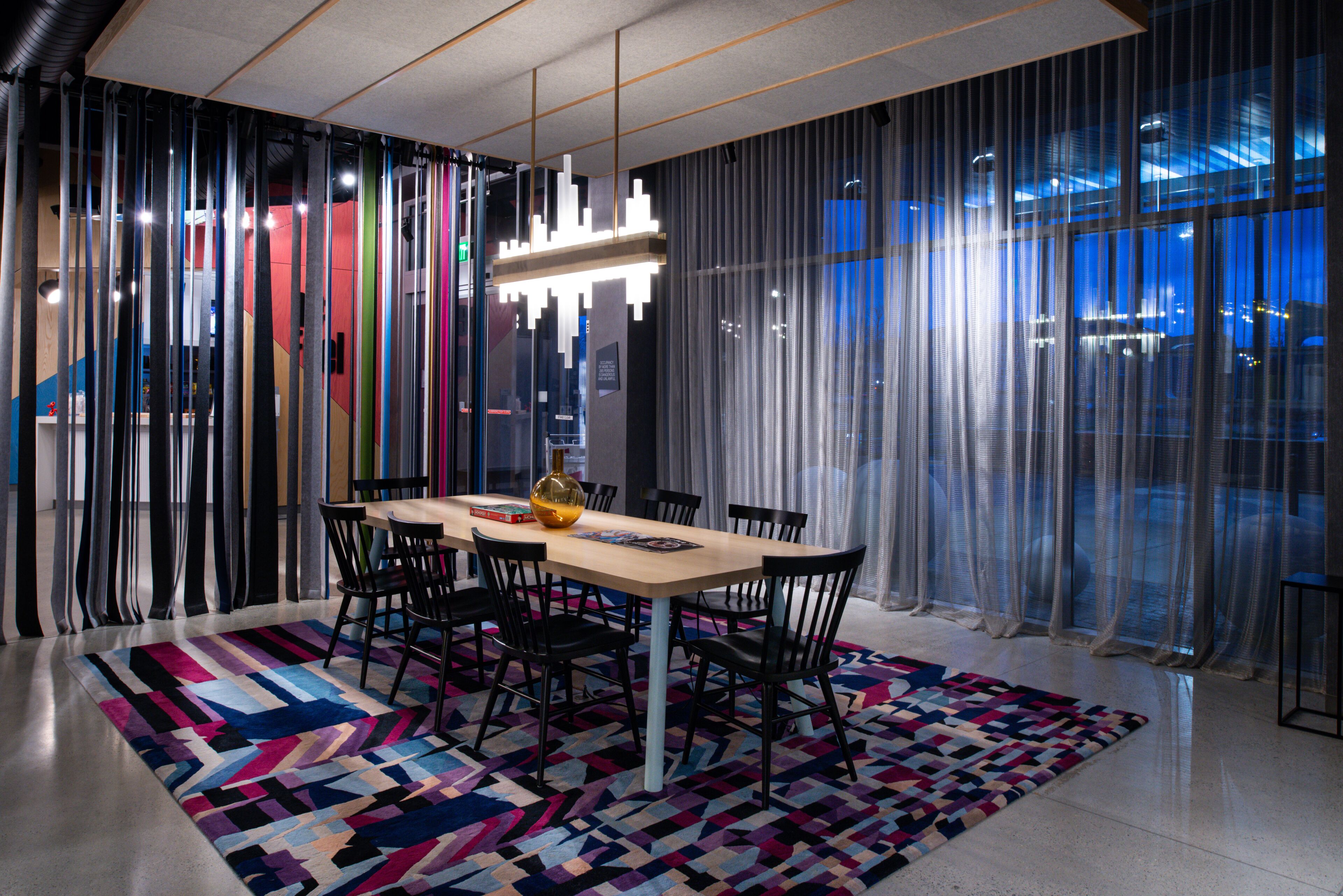 A modern dining area with a large table, chairs, and a colorful rug.