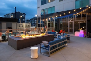 An outdoor seating area with a fire feature, modern furniture, and string lights.