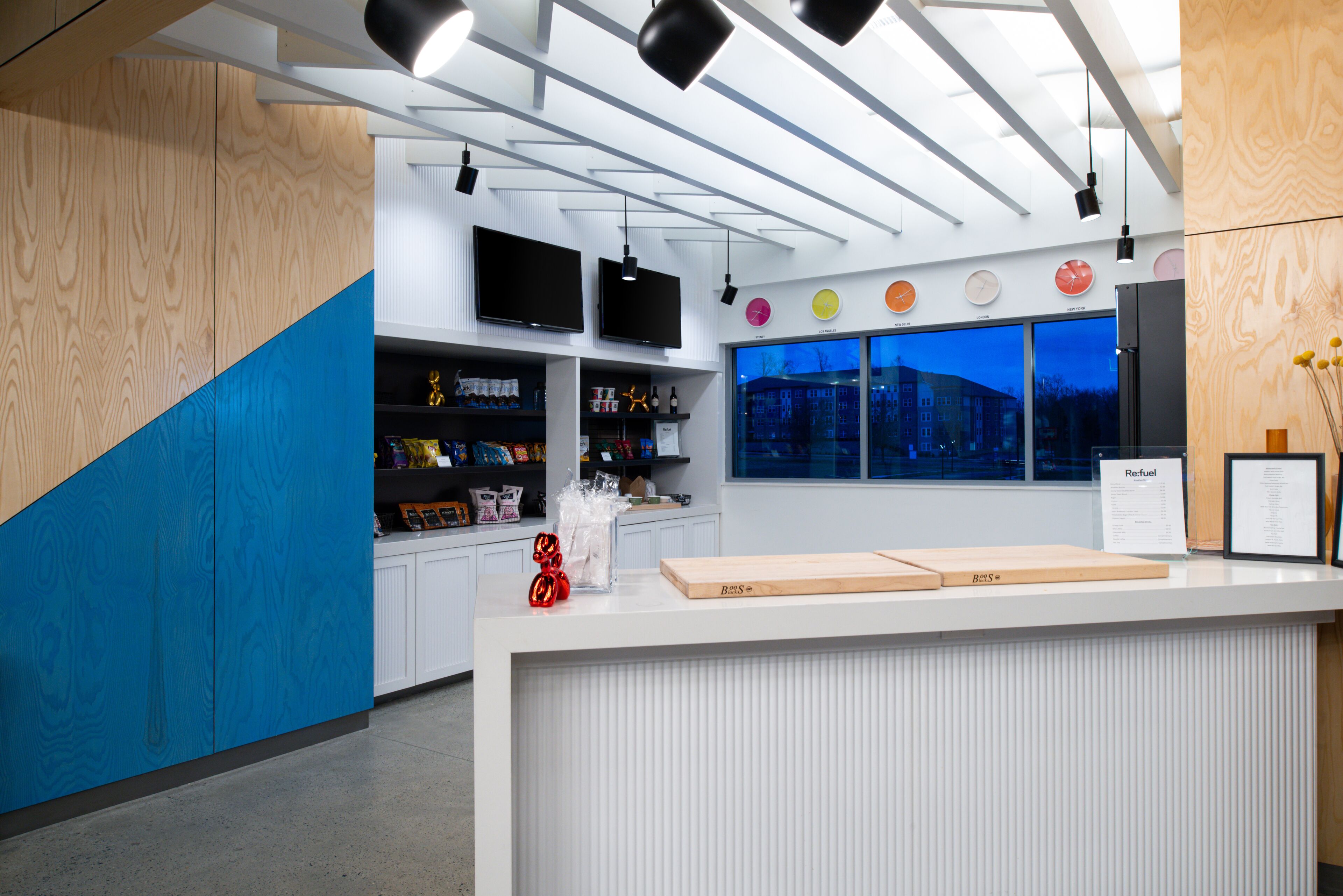 A modern reception desk with a wooden and blue design, a large window with a city view, and multiple screens above the desk.