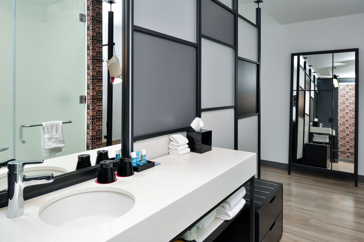 Un baño moderno con un espejo grande, lavabo blanco y un sujetatelas negro.