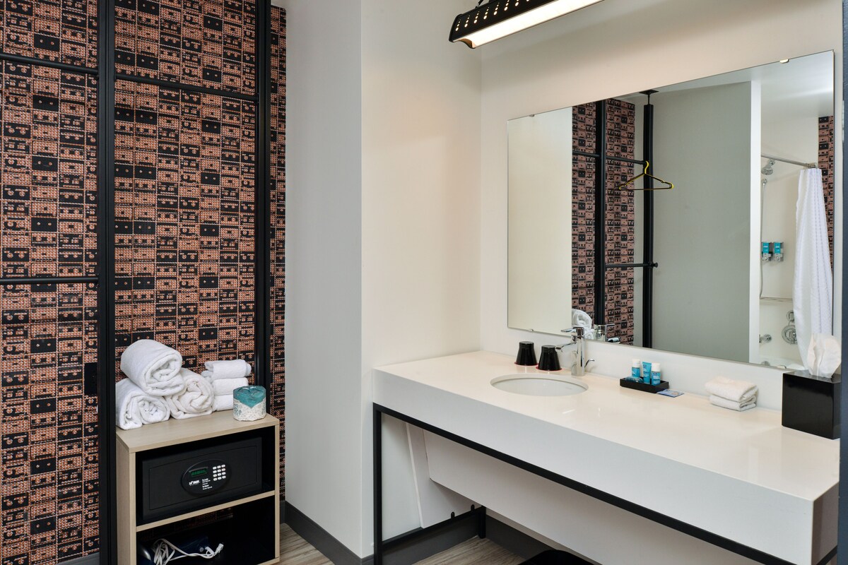 Un baño moderno con un lavamanos blanco, un espejo grande y un papel tapiz estampado.