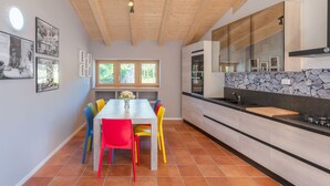 A modern kitchen with wooden beams, a dining area with colorful chairs, and a stone backsplash. - Villa in the vineyards overlooking the mountains (Rovereto)
