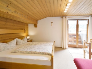 Ein Zimmer mit Holzwänden, einem Bett, einem Kreuz an der Wand und Blick durch eine Glastür.