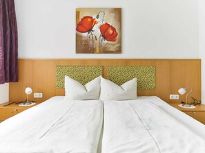 Een tweepersoonsbed met witte lakens, een hoofdbord met een groen patroon en een schilderij van rode bloemen aan de muur.