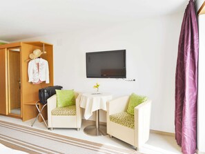 Ett hotellrum med en säng, en tv, två stolar, ett litet bord och ett fönster med gardiner.