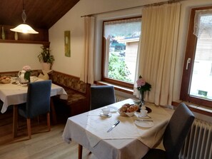 Un coin repas avec une table dressée pour deux personnes, un banc et une vue sur l’extérieur.
