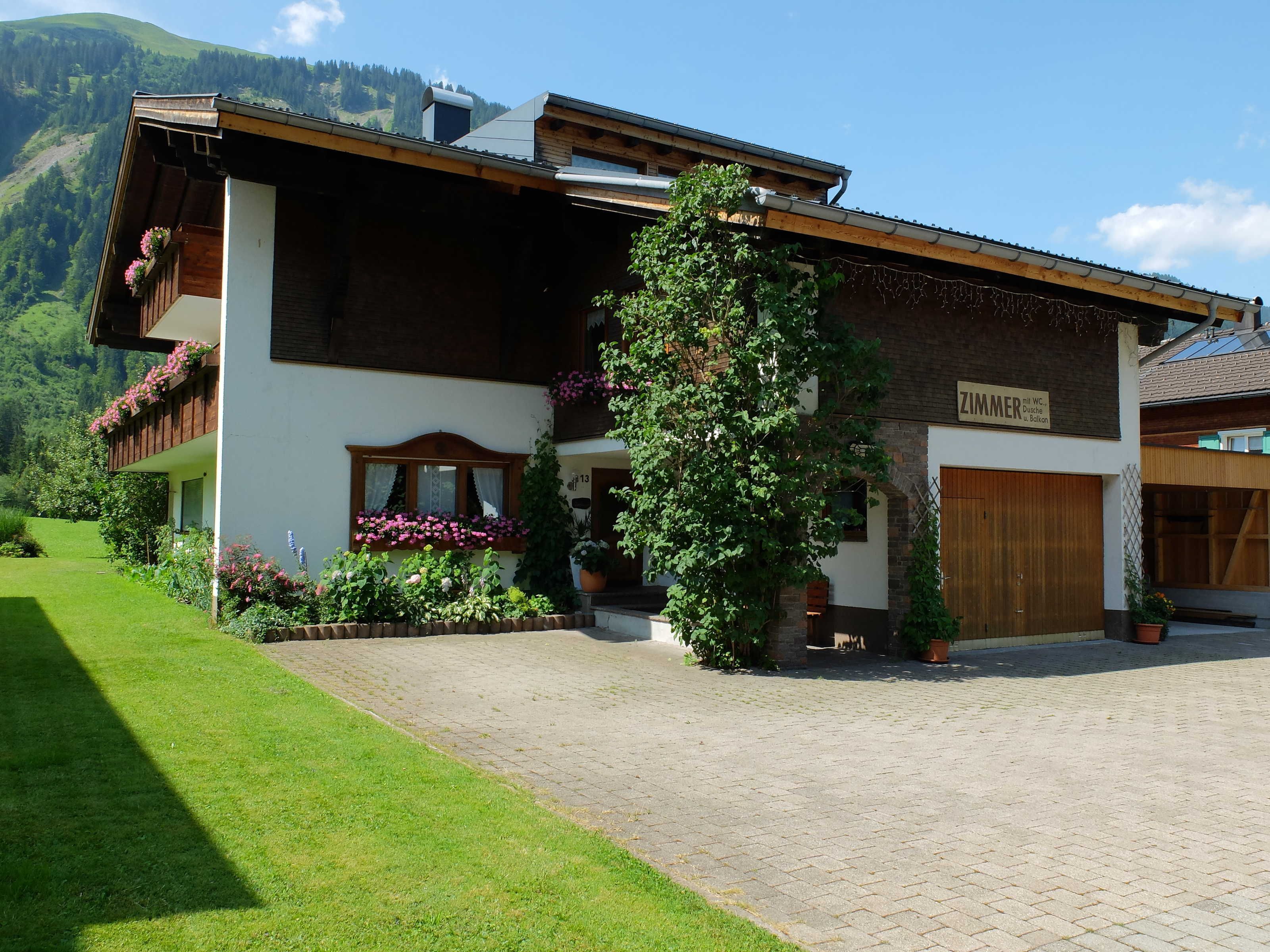 A two-story building with a wooden facade, a balcony with flower boxes, and a sign indicating a room number.