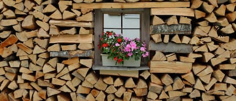 A stack of firewood with a window displaying flowers.