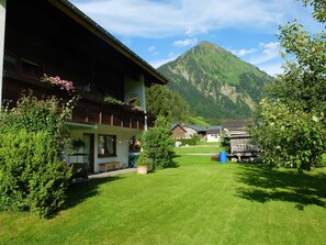 A traditional chalet with a balcony, a well-maintained lawn, and a mountain backdrop.