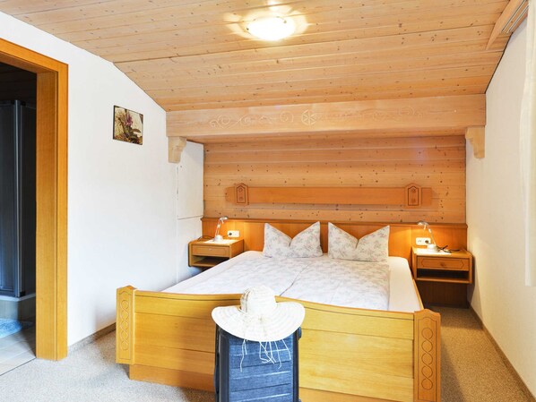 Een houten bed met hoofdeinde, twee nachtkastjes en een bijzettafeltje met een lamp.