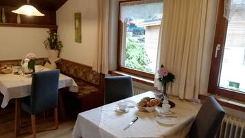 A dining area with a table set for two, a bench, and a view of the outside.