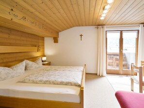 Una habitación con paneles de madera, una cama, una cruz en la pared y vistas a través de un ventanal.