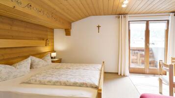 A wooden-paneled room with a bed, a cross on the wall, and a view through a glass door.