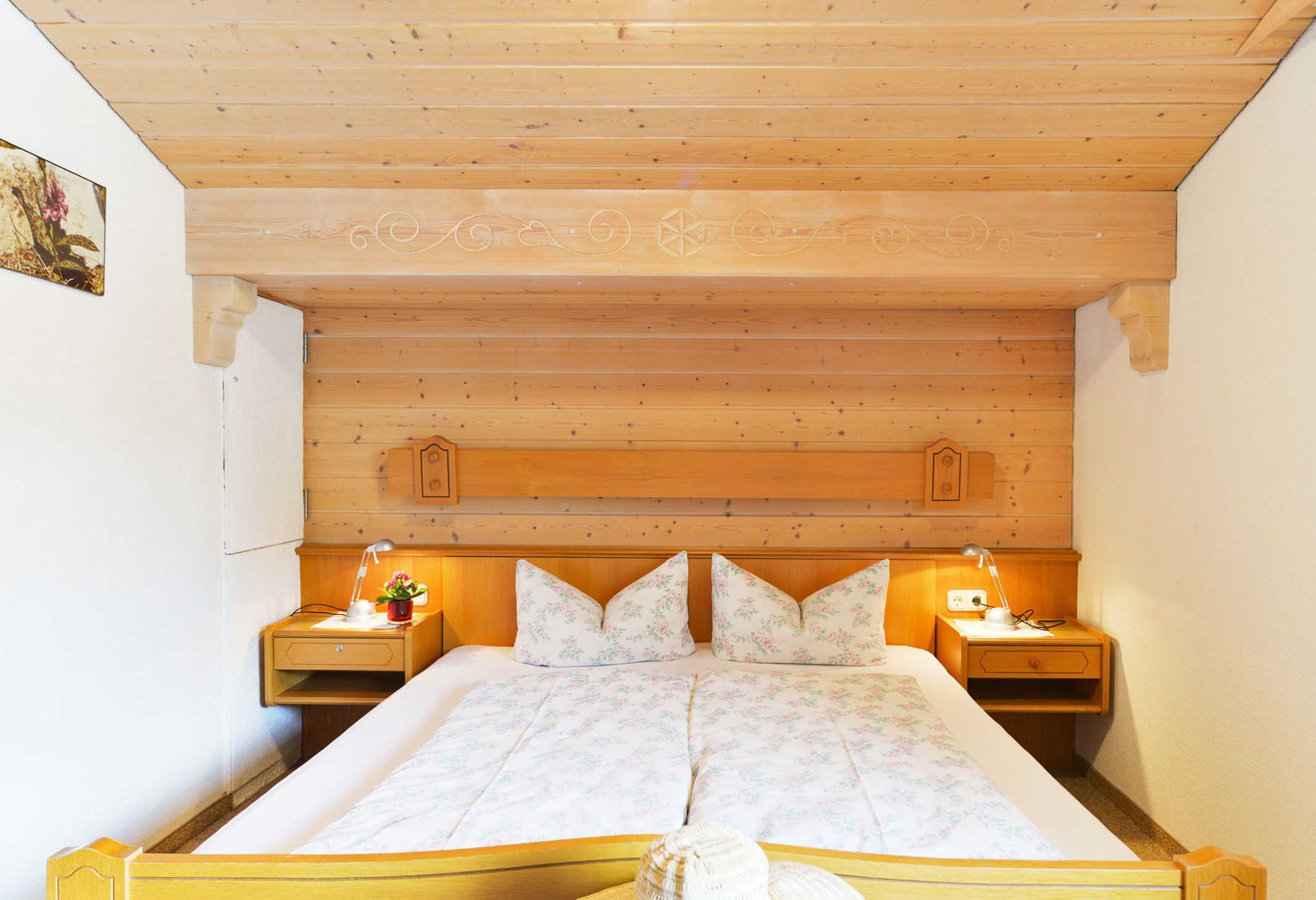 A wooden-paneled room with a bed, two bedside tables, and a wall-mounted shelf.
