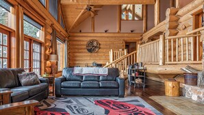 A log cabin interior with a leather sofa, wooden walls, a large rug, and a staircase. - Spirit Lodge at Silverstar (Vernon)