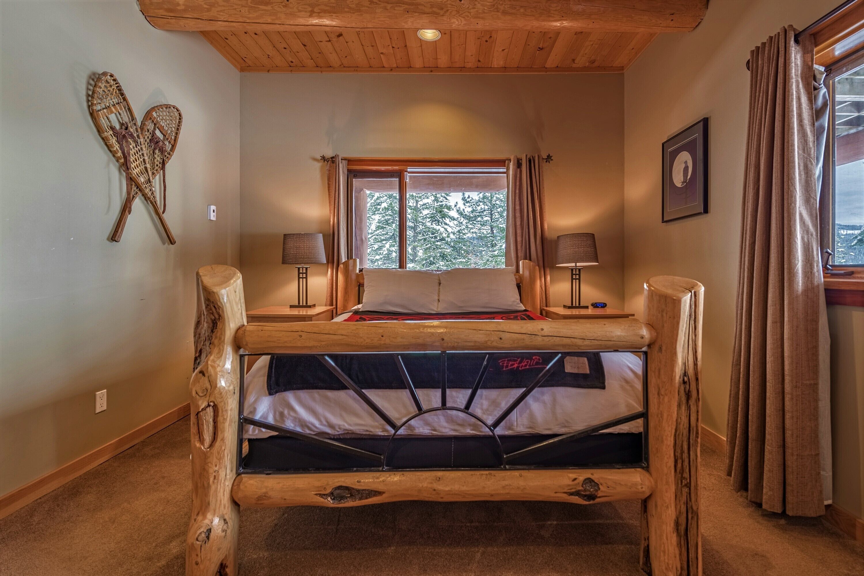 A rustic wooden bed with a headboard, a window with curtains, and two bedside lamps.