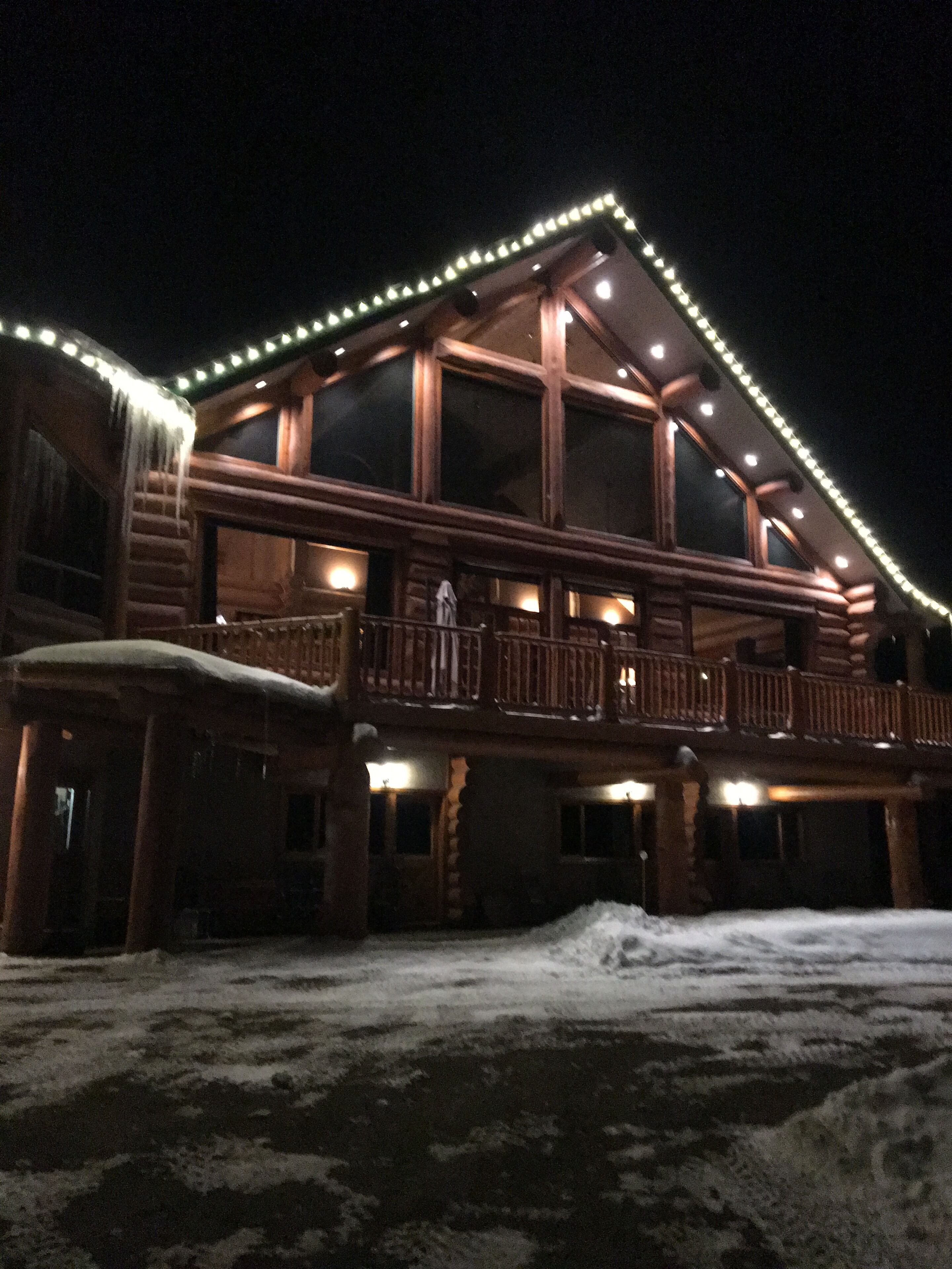A large log cabin with a balcony and a covered entrance, surrounded by snow.