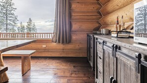 A wooden cabin interior with a wooden bench, a dining table, a kitchen area with cabinets and a stove, and a view of trees through a window. - Spirit Lodge at Silverstar (Vernon)