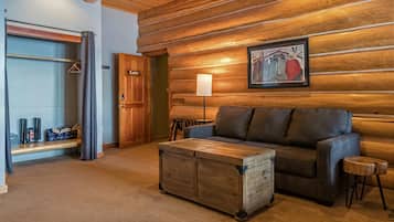 A log cabin interior with a sofa, a wooden chest, a lamp, and a coat rack.