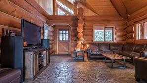 A log cabin interior with a stone floor, wooden walls, a leather couch, a TV, and a fireplace. - Spirit Lodge at Silverstar (Vernon)