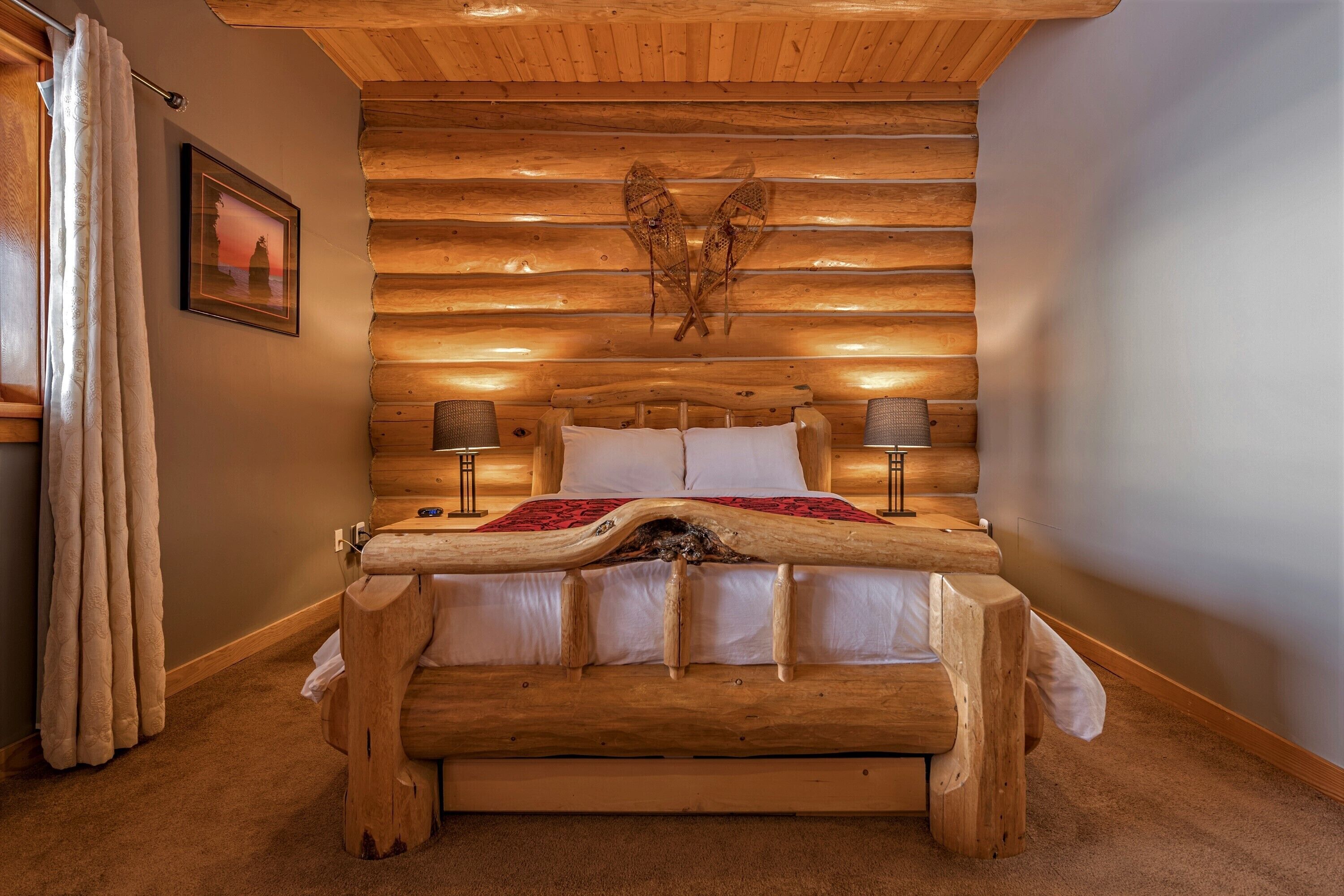 A wooden bed with a carved headboard, two bedside lamps, and a framed picture on the wall.