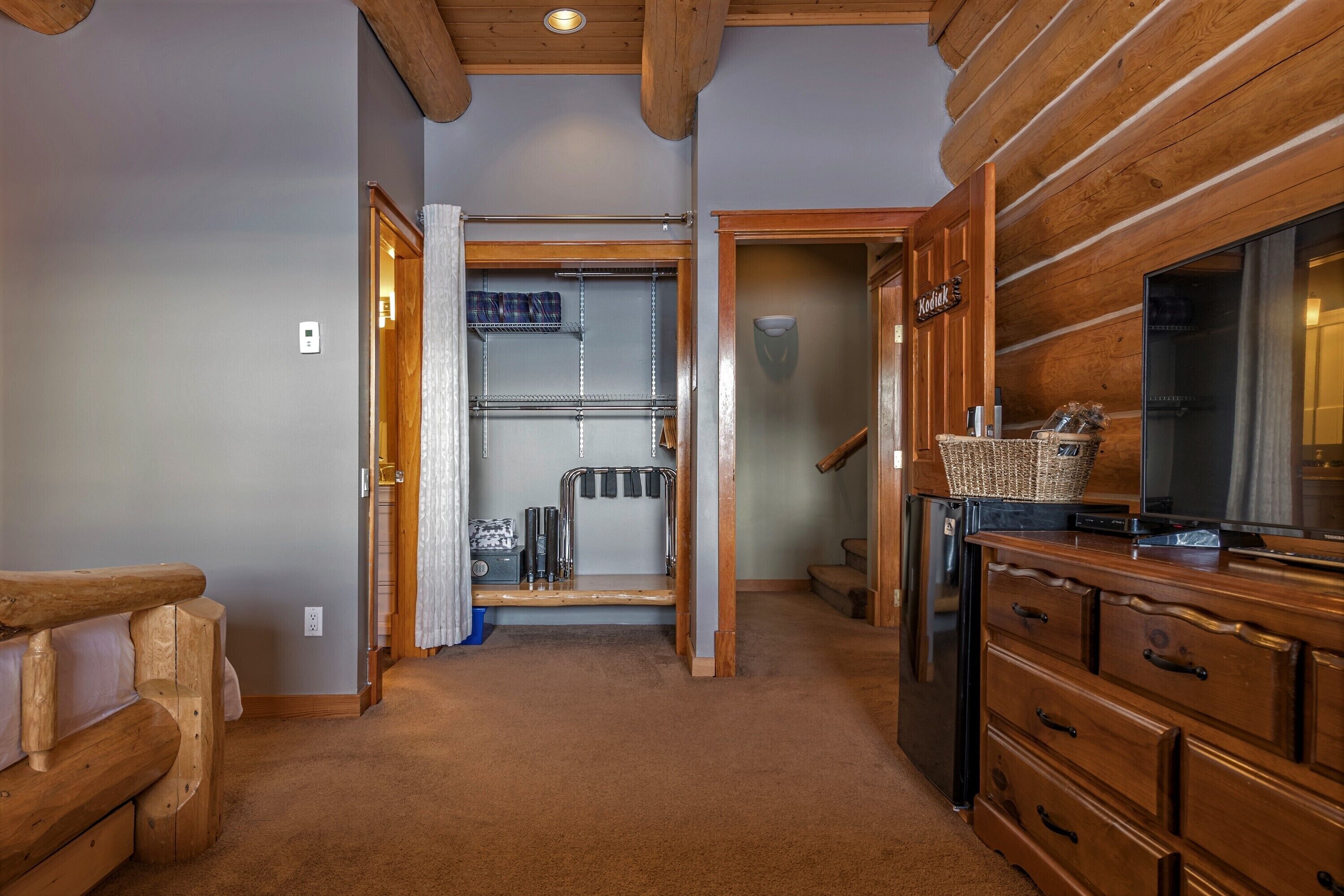 A hallway with a wooden bench, a wooden cabinet with drawers, a television, and a closet with a metal shelf and a basket.