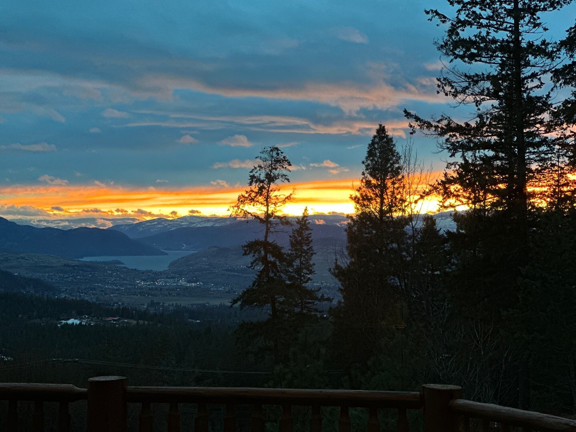 A scenic view from a balcony with a railing, overlooking a valley and mountains during sunset.