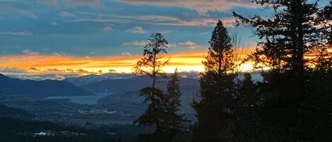 A scenic view from a balcony with a railing, overlooking a valley and mountains during sunset.