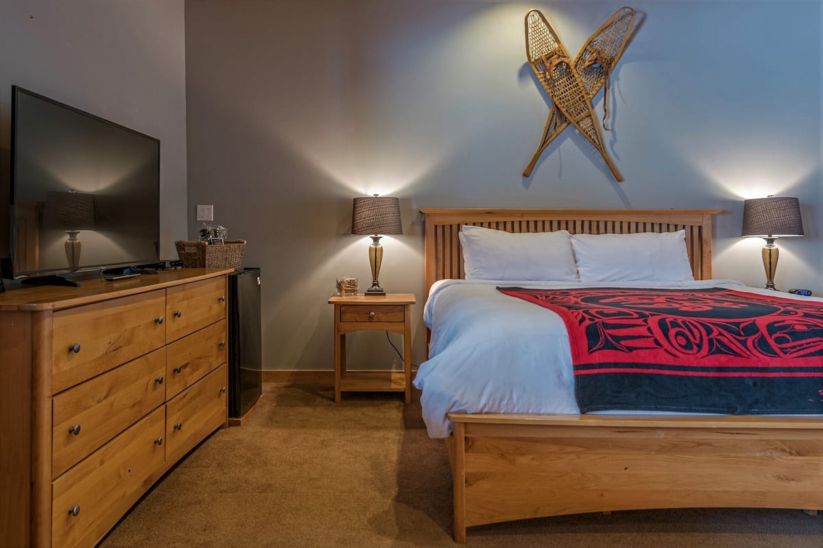A bedroom with a wooden bed, two bedside tables with lamps, a television on a dresser, and a wall-mounted decorative item.