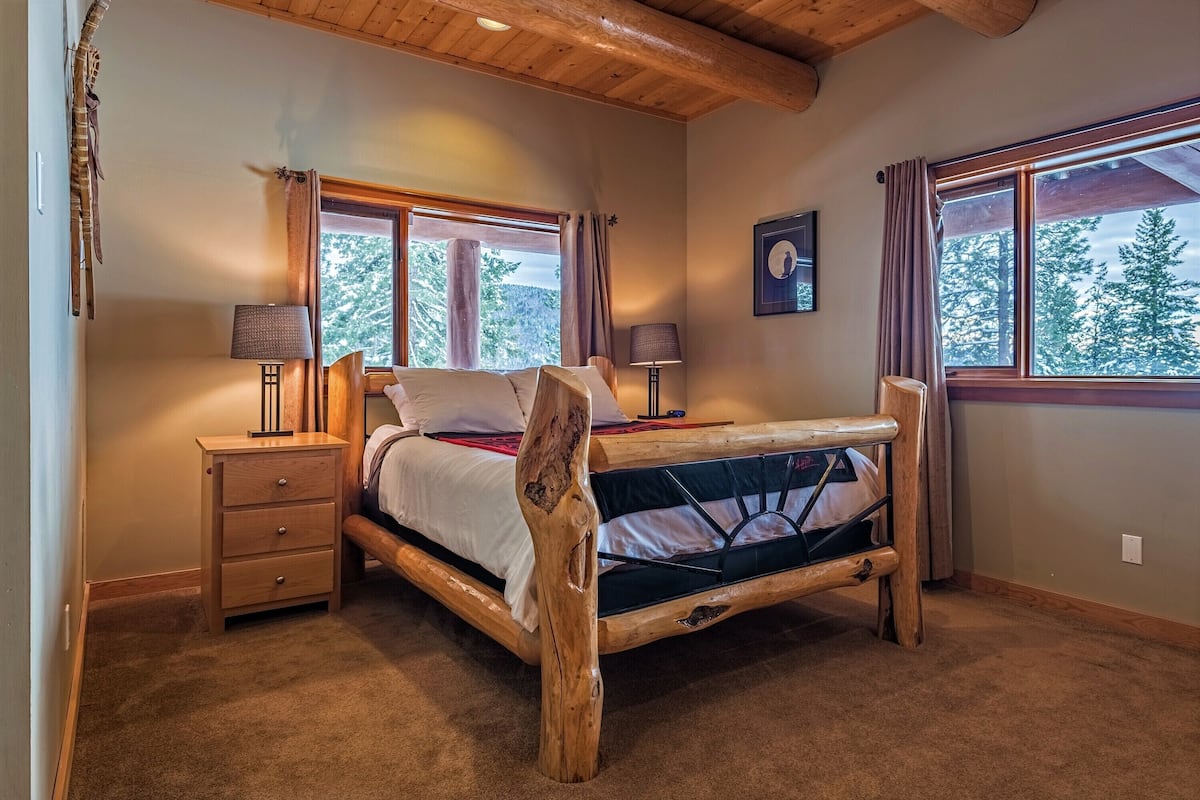A bedroom with a wooden bed frame, two bedside tables, a nightstand, and a window with curtains.