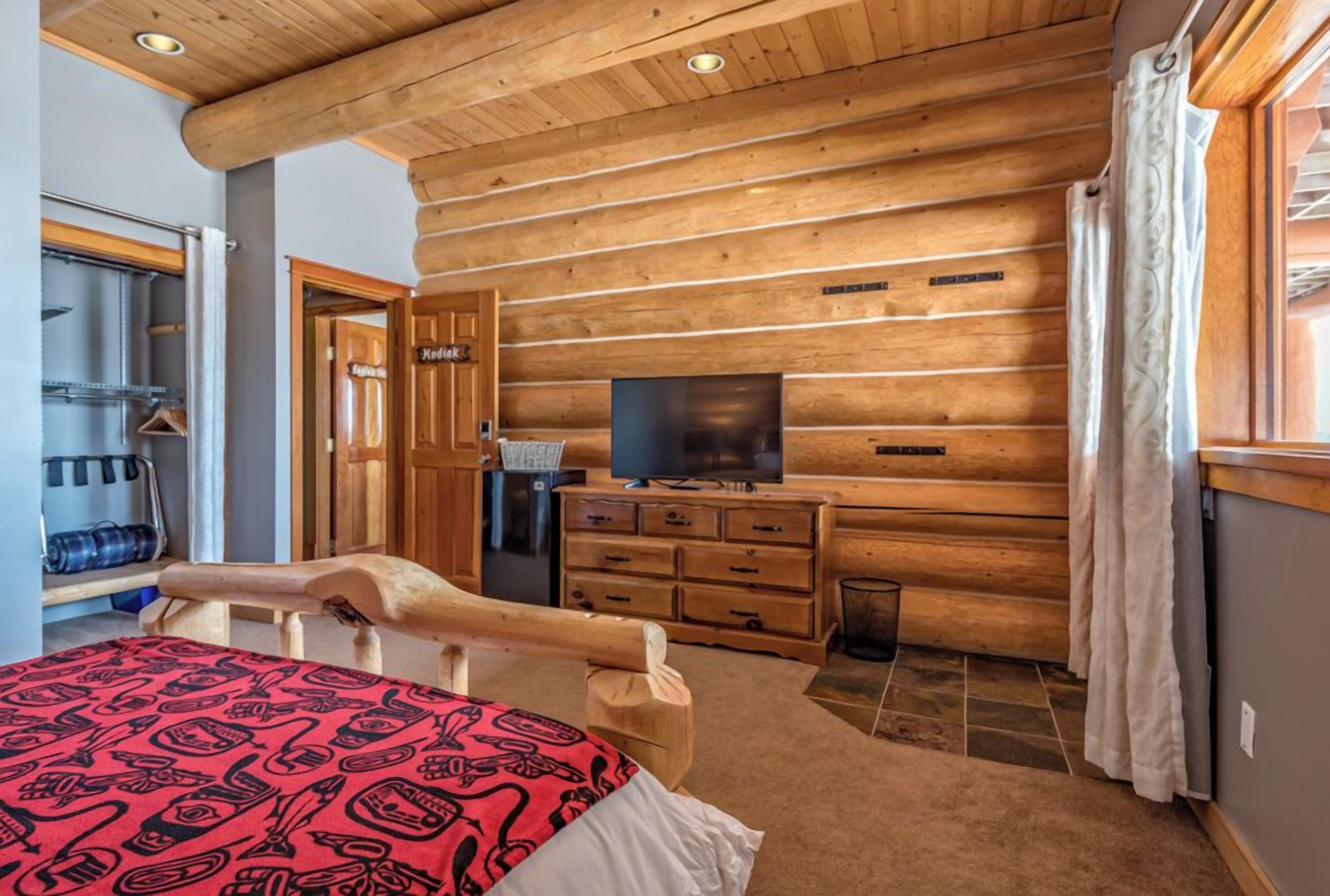 Une chambre située dans un chalet en rondins, comprenant un lit, une commode en bois, une télévision et un espace douche.