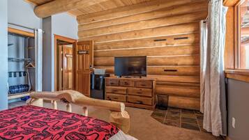 Une chambre située dans un chalet en rondins, comprenant un lit, une commode en bois, une télévision et un espace douche.