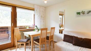 A cozy room with a dining table, chairs, a sofa, and a window with curtains.