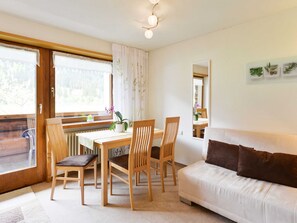 Een knus ingerichte kamer met een eettafel, stoelen, een bank en een raam met gordijnen.