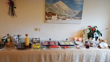 A buffet table with various food items, condiments, and a painting of a mountain landscape on the wall.