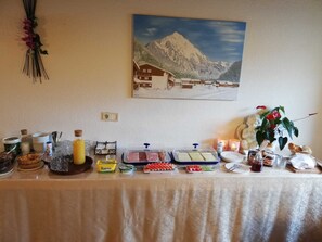 Een buffettafel met diverse gerechten, sauzen en een schilderij van een berglandschap aan de muur.