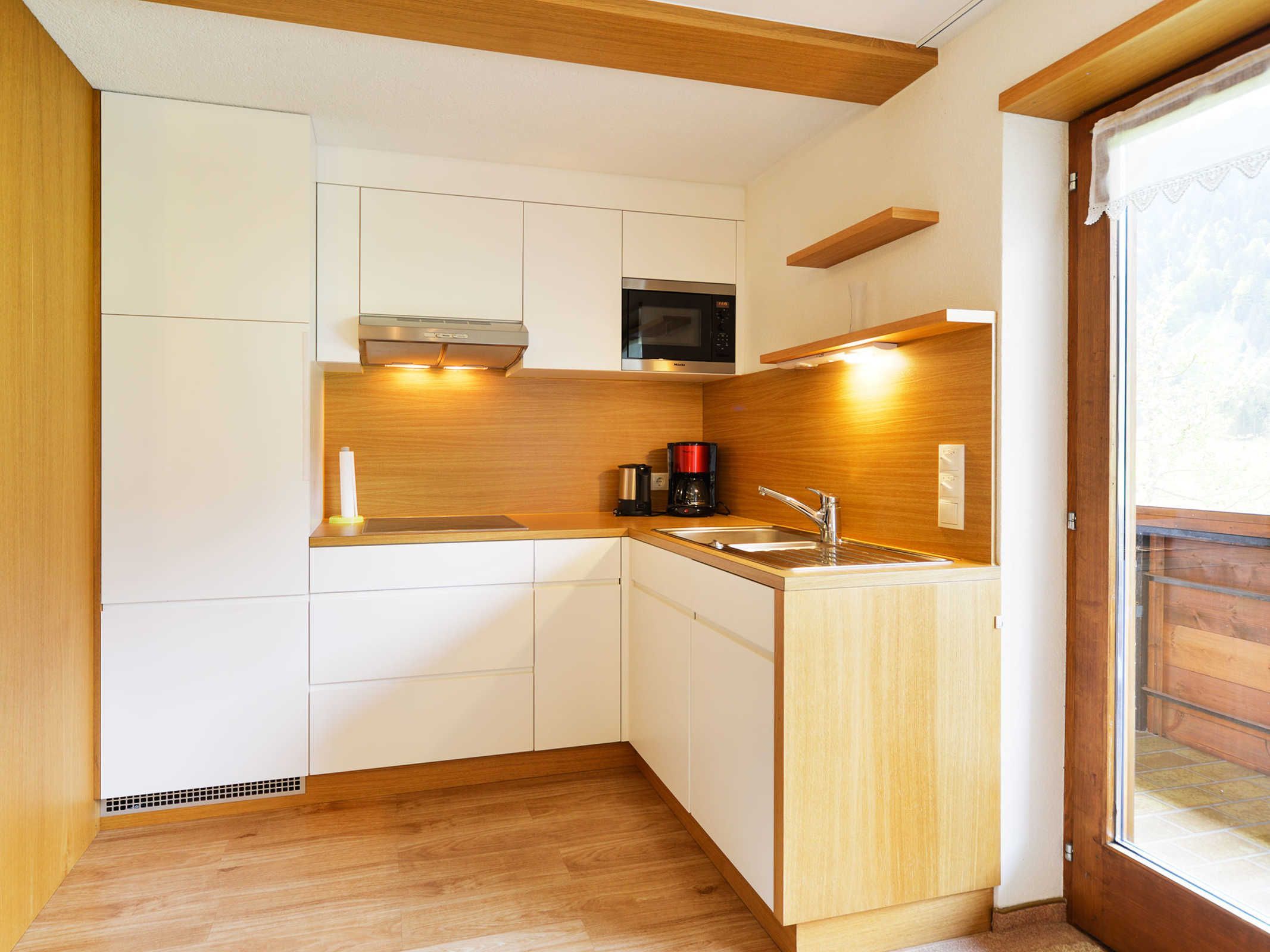 A compact kitchen with white cabinets, a microwave, a coffee maker, and a sink.