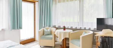 A hotel room with two armchairs, a small table, a TV, and a bed.