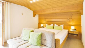 Une chambre avec un plafond en bois, un lit avec des oreillers verts, une table de chevet avec une lampe et une fenêtre avec des rideaux.