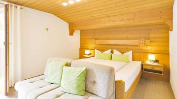 A bedroom with a wooden ceiling, a bed with green pillows, a nightstand with a lamp, and a window with curtains.