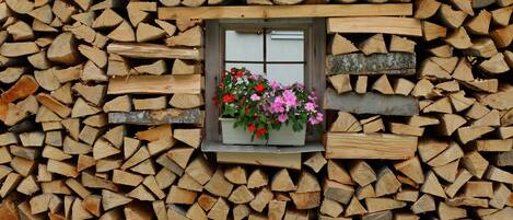 A stack of firewood with a window displaying flowers.