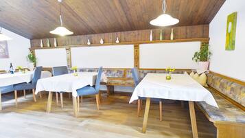 A restaurant with wooden ceiling, white tables, blue chairs, and a bench.